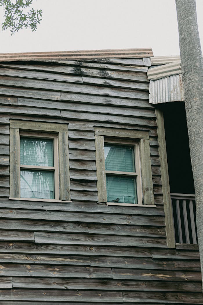 Weathered wooden cottage with green framed windows and corrugated metal roof detail.